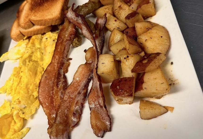 A brunch plate with scrambled eggs, bacon, home fries, and toast