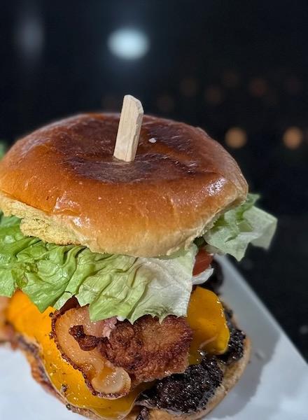 A loaded burger with bacon, roasted peppers, and lettuce on a toasted bun