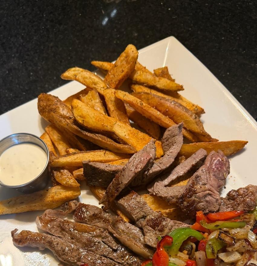 Sliced steak with roasted peppers, onions, and seasoned fries